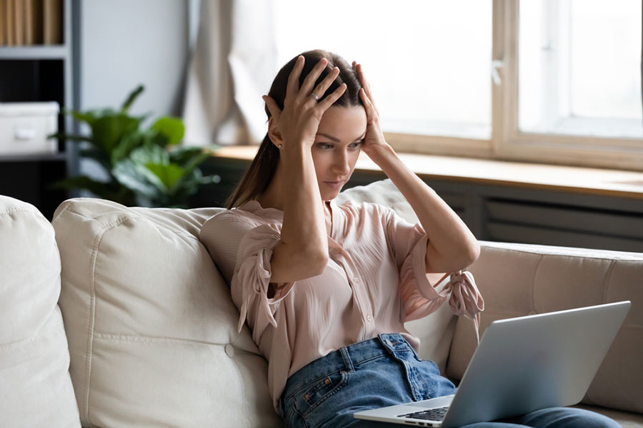 Une personne inquiète avec les mains sur la tête devant son ordinateur portable.